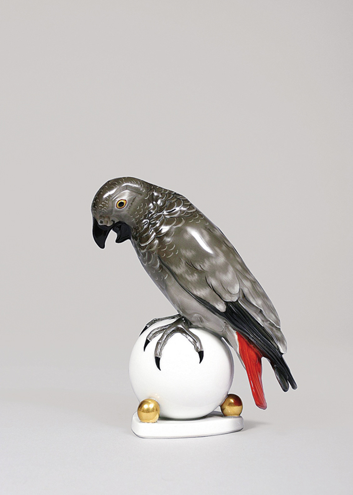 An animal figure of a grey parrot seated on a ball