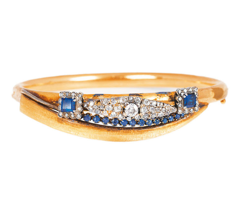 A golden bangle bracelet with diamond and sapphire setting