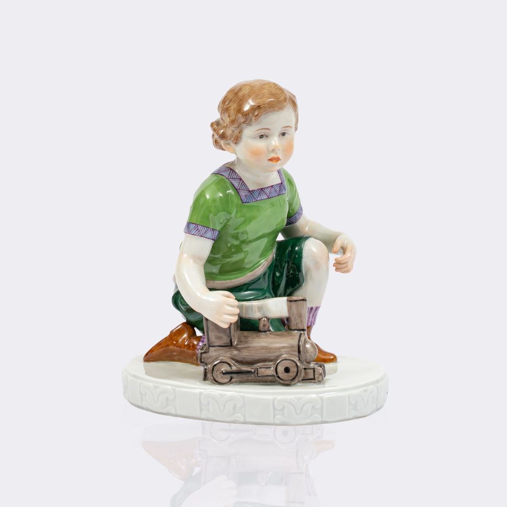 Kniender Junge mit Lokomotive und Ball