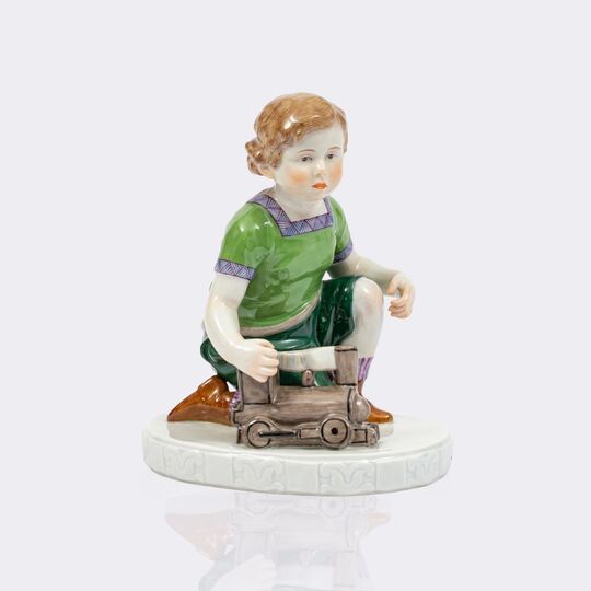 Kniender Junge mit Lokomotive und Ball